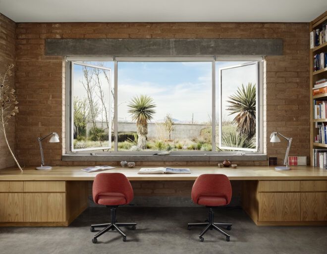 A long desk that covers the entirety of one wall facing an open window