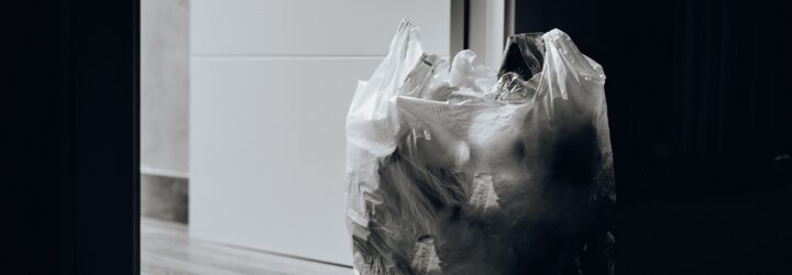 A black and white photo of a plastic bag filled with plastic bottles sitting by a doorway