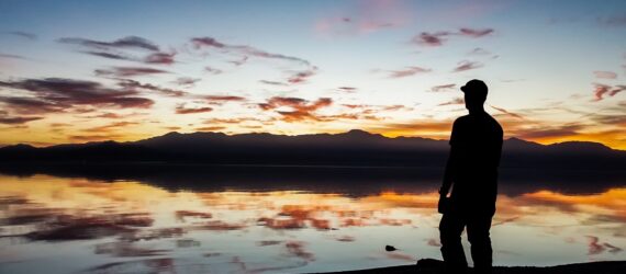 A silhouette of a person standing on the edge of a river