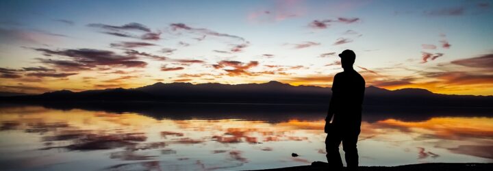 A silhouette of a person standing on the edge of a river