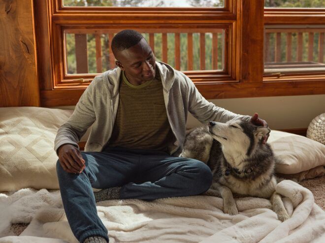 A man sitting on a bed with a husky