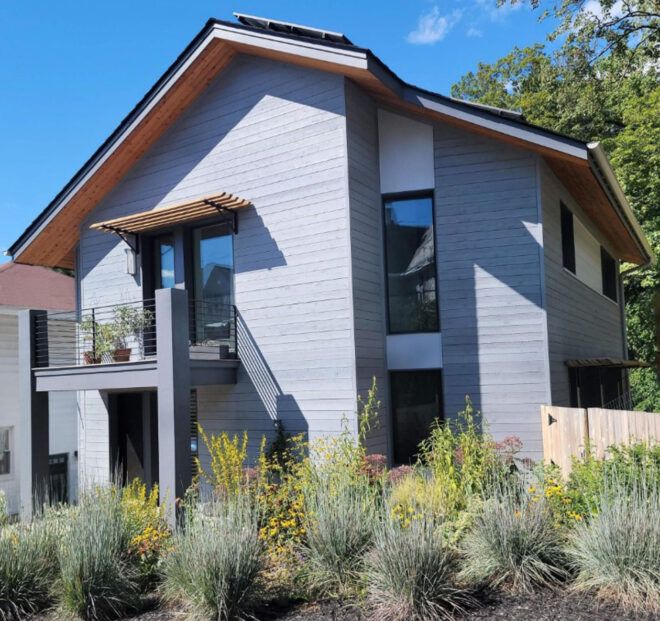 Brush outside of a light gray home with slanted roof