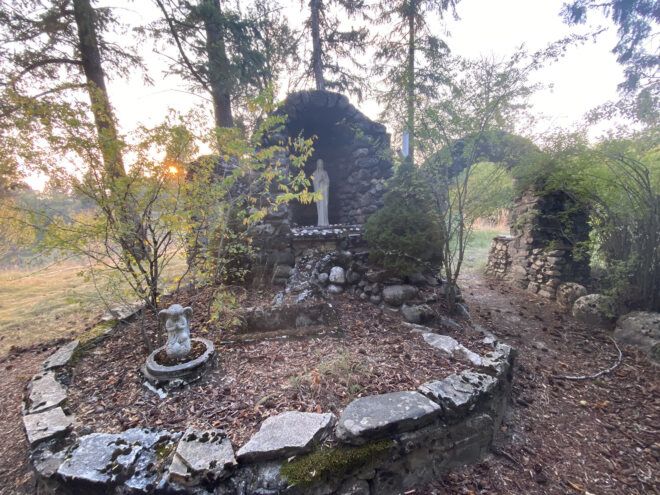 A stone garden with sculptures and an archway in a forest