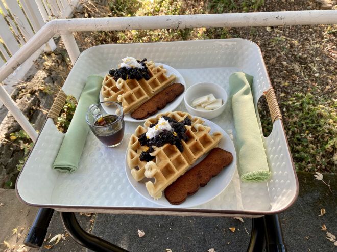 A tray with two plates of waffles, a rolled up green napkin and a cup of juice