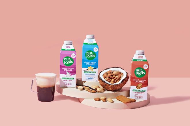 Three dairy free coffee creamers in packaging of purple, blue and red against a pink background