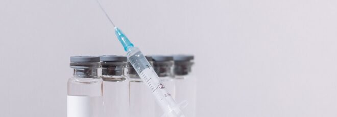 A syringe leaning on five clear glass vials