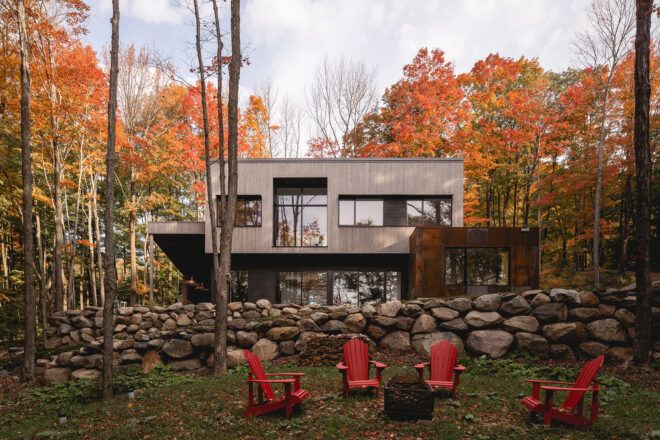 A modern designed two-story home with a stone wall to separate a camping area with red chairs