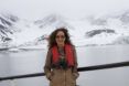 A woman wearing an orange life vest with a glacier backdrop behind her