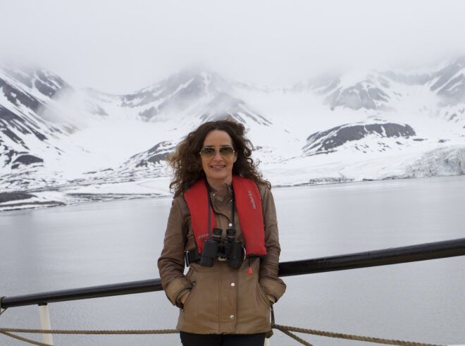 A woman wearing an orange life vest with a glacier backdrop behind her