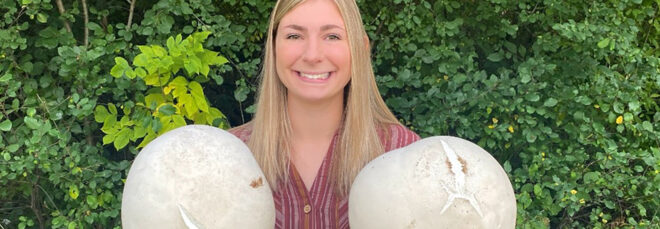 A woman holding two giant puffball mushrooms in each hand