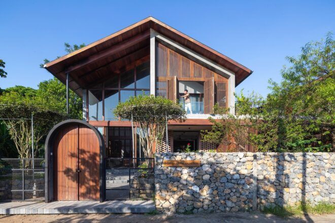 A wooden two-story home with a wooden door out front connected to a stone wall