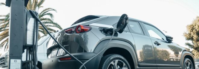 A gray electric vehicle plugged into an EV charging station outdoors