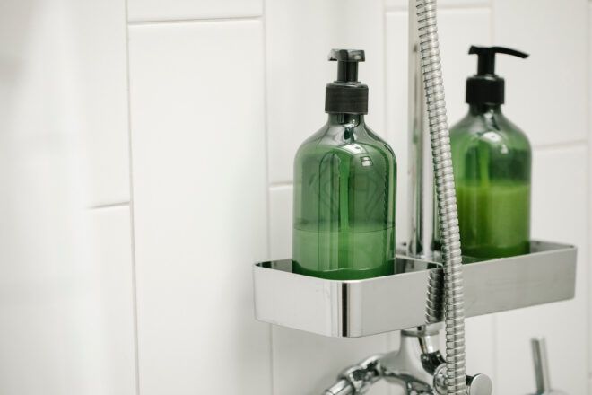 Two green shower bottles in a shower container against white tiles