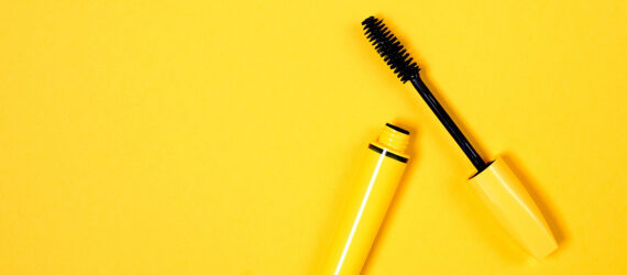 A yellow mascara with the top off against a yellow background