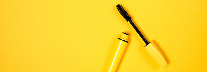 A yellow mascara with the top off against a yellow background