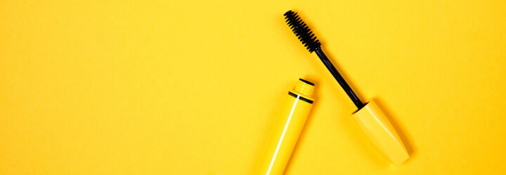 A yellow mascara with the top off against a yellow background