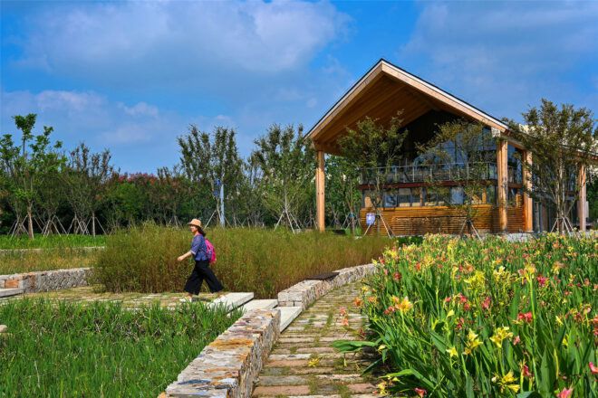 A wooden house within a garden and a person walking along a path in front of it