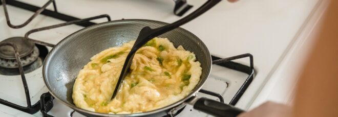 A spatula stirring around eggs in a pan on a stove