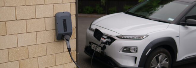 A white electric car plugged to a charging port attached to a brick wall