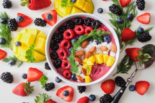 A fruit smoothie bowl and laid outside of the bowl fruits such as mango, strawberry and blueberries