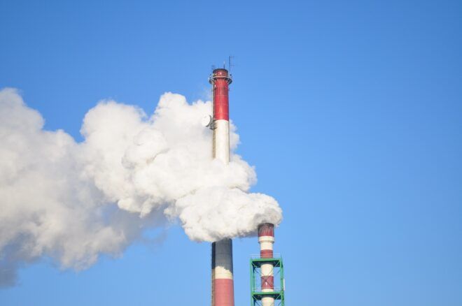 Two pipes with white steam billowing out of it against a blue sky