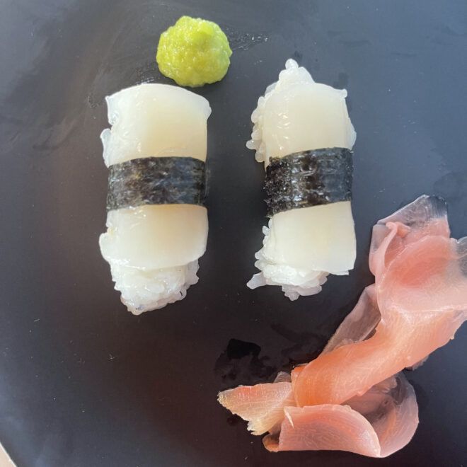 Plant-based white fish nigiri with wasabi and pickled ginger on a black plate