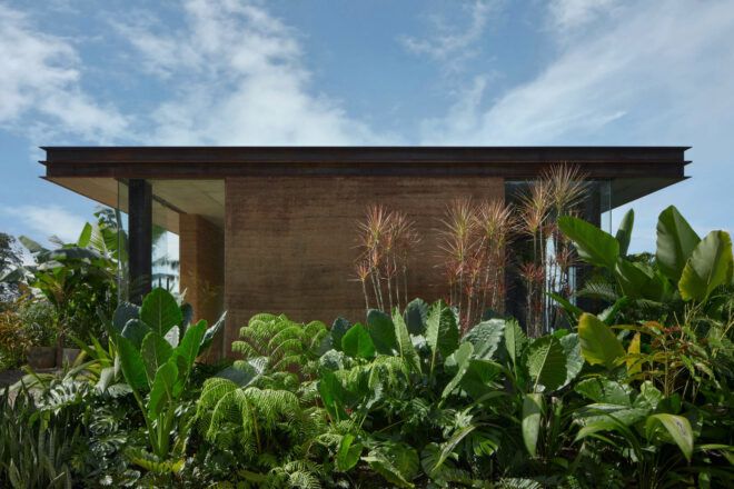 Side facade of a villa featuring rammed earth walls flanked by lush greenery