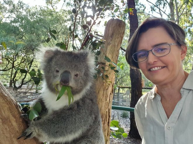 A woman wearing glasses and short hair standing beside a koala
