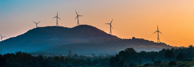 A hill landscape during evening time with wind turbines on top of the hill