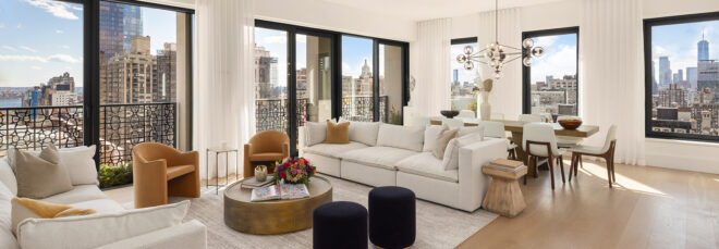A living room space with windows encompassing to overlook the skyscraper and city landscape outside