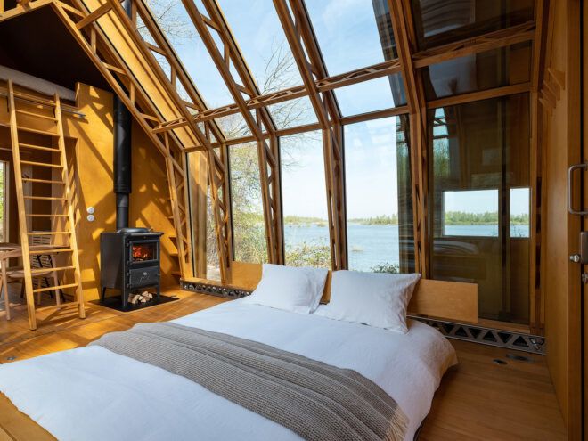 Interior of a cabin with a bed beside a fireplace and open windows