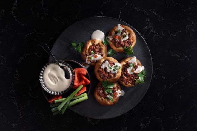 Open-faced pastries with fresh veggies and a dip cultured meat mince on a black plate with veg