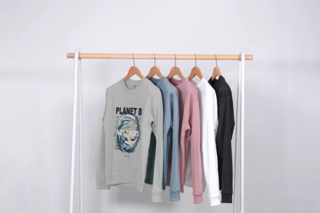 A rack of clothes of a sweater with a planet design on it in colors of gray, blue, pink, white and black