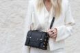 A crossbody black purse across the torso of someone wearing a white blazer