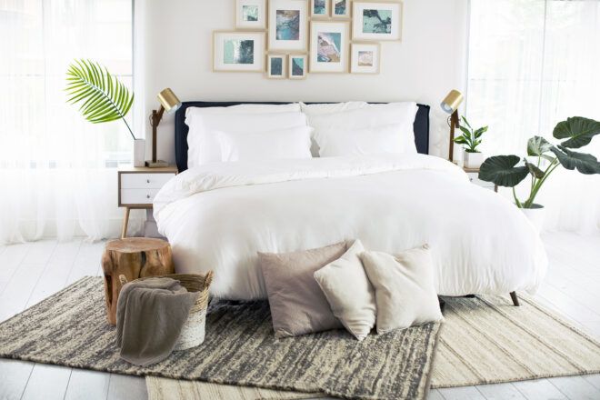 A white bed with pillows and sheets at the ground at the foot of the bed