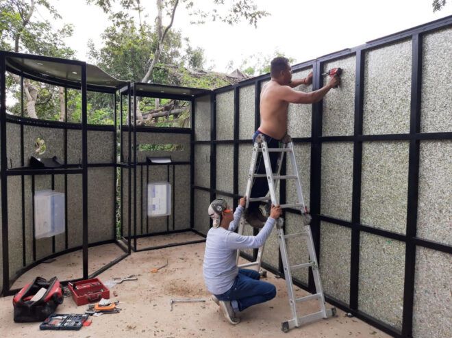 Two people working on assembling a wall of a low building