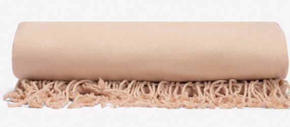 A tan rolled throw blanket with fringe ends