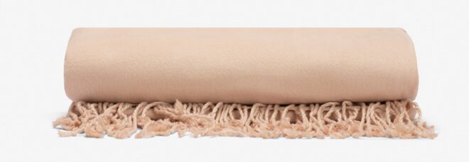 A tan rolled throw blanket with fringe ends