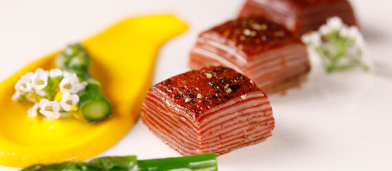 Three 3D-printed Omakase Beef Morsels on a white plate with a yellow sauce and asparagus