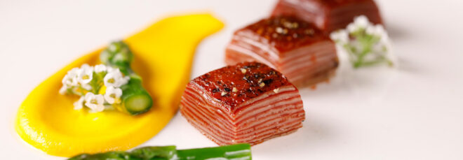 Three 3D-printed Omakase Beef Morsels on a white plate with a yellow sauce and asparagus