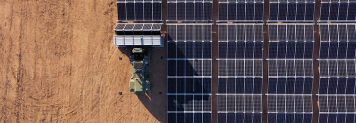 A tractor folding out solar panels on a dirt land