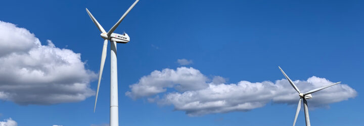 Two wind turbines against a blue and cloud sky