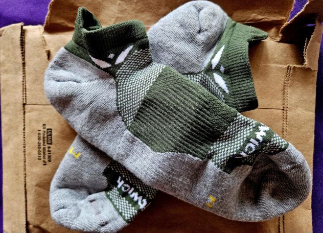 Two dark green and gray socks laid across each other on a packaging