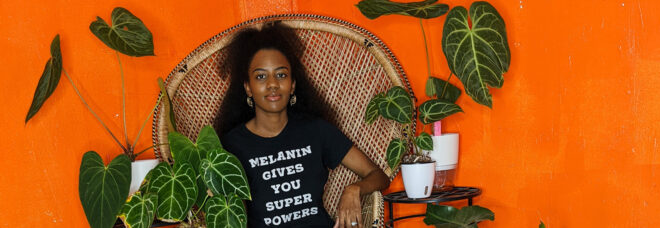 A black woman sitting in a wicker chair surrounded by plants