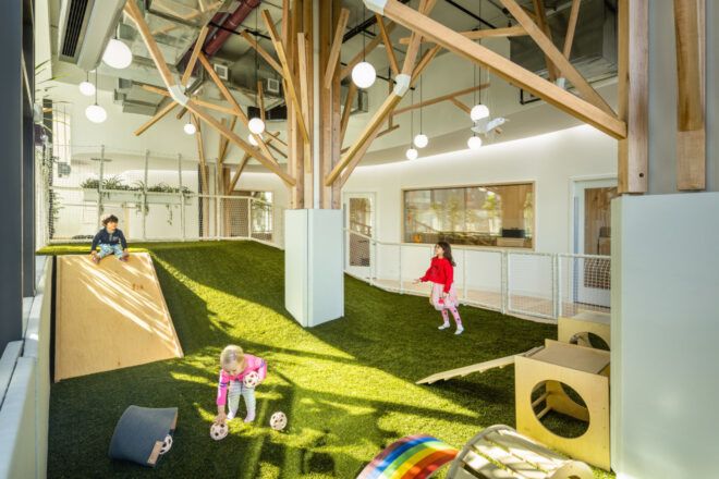Children playing in an indoor forest space with a hilly landscape and abstracted wooden trees