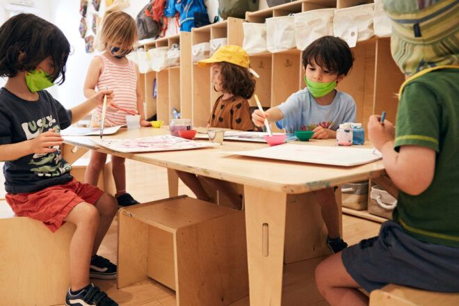 Five preschoolers on one wooden table, painting on canvas boards