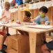 Five preschoolers on one wooden table, painting on canvas boards