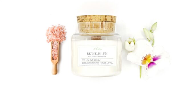 A candle with a cork lid set in between a scoop of salt and orchids