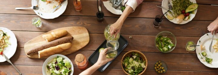 Two arms clinking cups in the center of a table filled with food