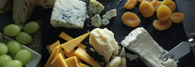 A charcuterie board with a variety of cheeses, grapes and dried fruits